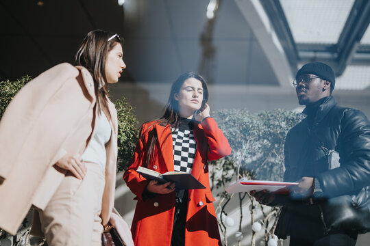 A multiethnic trio of coworkers in stylish attire are deep in conversation under natural light, depicting a modern, inclusive work environment.