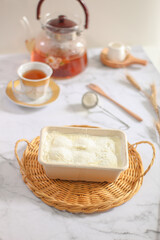 Milk Bun Thailand is a soft bread with a topping of powdered sugar, milk and vla filling,soft focus texture, served on rattan tray and cup of tea with a piece of bun. makanan viral indonesia