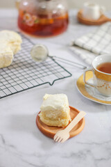 Milk Bun Thailand is a soft bread with a topping of powdered sugar, milk and vla filling, soft focus texture, served on black tray and cup of tea with a piece of milk bun. makanan viral indonesia