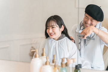 Fototapeta na wymiar 美容室で髪の毛を切る美容師・スタイリストと若い女性客 