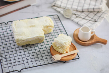 Milk Bun Thailand is a soft bread with a topping of powdered sugar, milk and vla filling, soft focus texture, served on black tray and cup of tea with a piece of milk bun. makanan viral indonesia