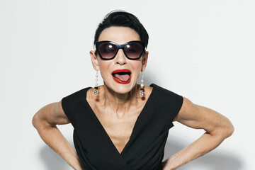 Stylish woman in sunglasses and black dress posing with hands on hips and mouth open