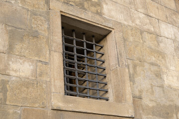 Iron grilles adorn the windows of an old building's wall, evoking the concept of an old prison and confinement.