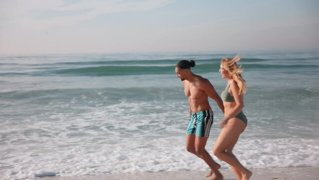 Young couple in swimwear having fun on summer vacation holding hands and running along beach in South Africa - shot in slow motion