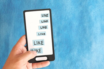 Hand holding a mobile phone paper cutout hitting word like. Social media concept.