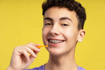 Handsome, smiling boy with braces using interdental brush, looking at camera. Attractive teenager