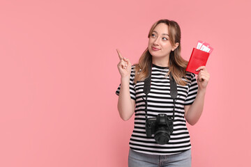 Happy young woman with passport, ticket and camera pointing at something on pink background, space for text