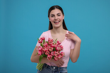 Happy young woman with beautiful bouquet on light blue background