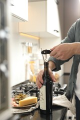 Man opening wine bottle with corkscrew at black countertop indoors, closeup