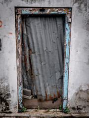 a damaged door covered with zinc boards in a house that has been abandoned by its owner
