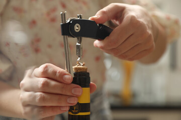 Woman opening wine bottle with corkscrew on blurred background, closeup