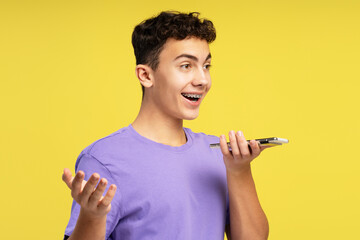 Portrait of attractive smiling boy, teenager holding mobile phone recording voice message
