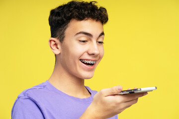 Portrait of handsome smiling boy, teenager holding mobile phone recording voice message