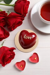 St. Valentine's Day. Delicious heart shaped cake, tea, roses and candles on white wooden table, flat lay