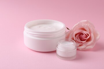 Moisturizing cream in open jars and rose flower on pink background. Body care product