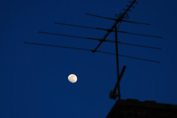 Moon with TV antenna against a deep blue evening sky. 