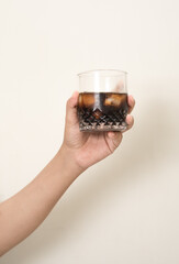 hand is holding a glass of coffee with ices on a white isolated background