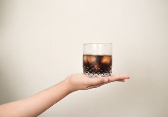 hand is holding a glass of coffee with ices on a white isolated background