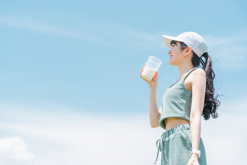 青空の下で運動中にプロテインを飲む若いアジア人女性
