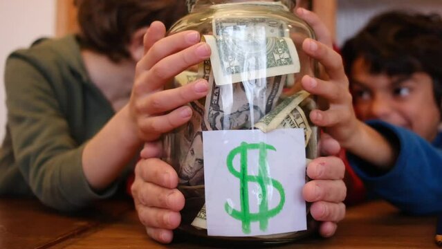 Siblings aged 6 and 8 keep dollar bills and save money in a glass jar. Concept of financial education, saving, investing with children and economy.