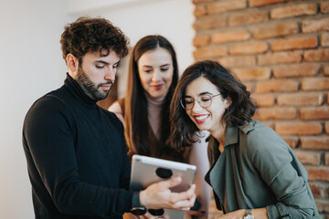 Three young professionals engaged in a discussion over a tablet, conveying teamwork and...