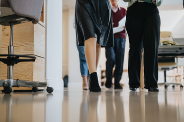 Low angle view capturing the stride of business professionals walking in tandem within a contemporary office corridor, reflecting a collaborative work environment.