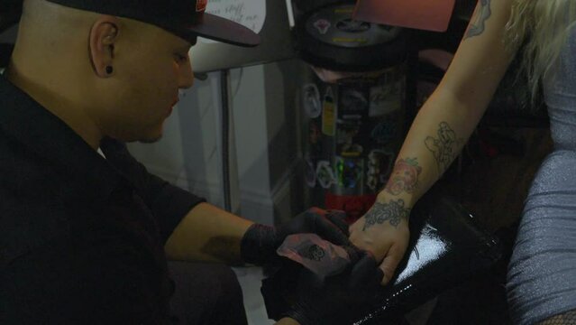 a male tattoo artist uses a tattoo pen to draw a tattoo onto the  back of clients hand