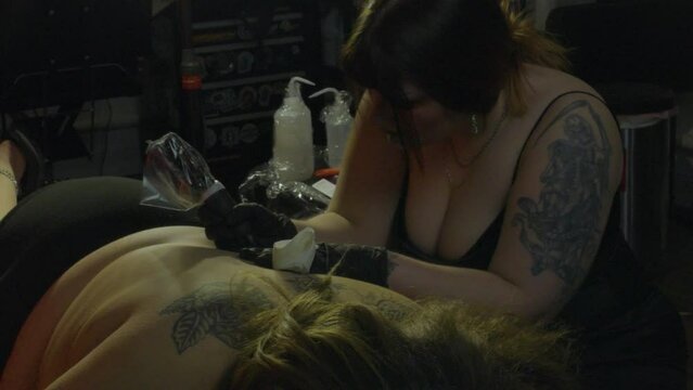 a female tattoo artist works intently at inking a tattoo on her clients back