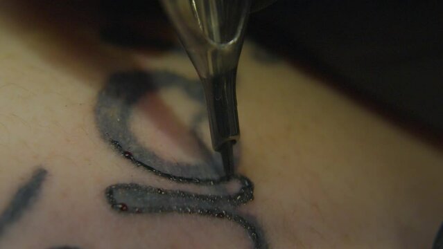 a fast moving tattoo needle inks the outline of an existing artwork causing droplets of blood to form on the surface of the skin