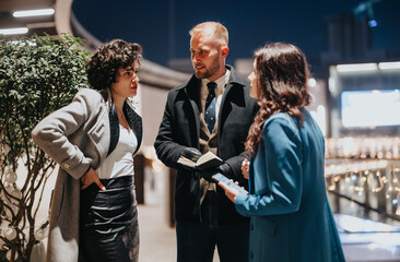 Three business partners actively discussing work during an evening networking event with urban lights in the background.