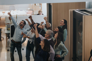 Ecstatic office team celebrating success with arms raised in victory.