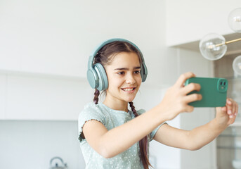 Cute nine year old girl wearing headphones holding a smartphone and taking a selfie, childhood and...