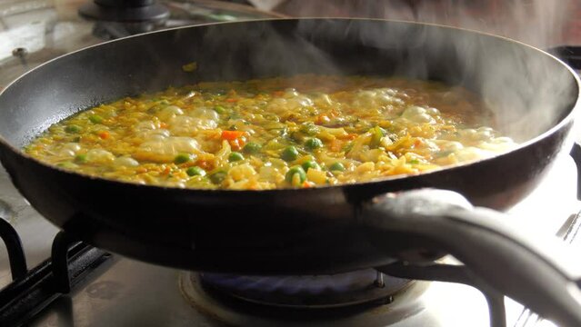 A large pan of bubbling risotto is boiling. Risotto with vegetables and pieces of chicken is prepared in the home kitchen