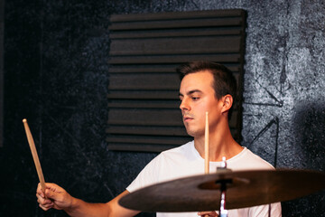Close-up of a concentrated young musician playing the drums in a music rehearsal room