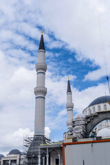 Tall minarets of a mosque under construction tower beside a crane against a cloudy sky, in Istanbul, Turkiye.