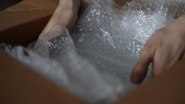 Close-up cropped shot of unrecognizable man putting breakable fragile glassware into cardboard box to moving to new house. Male packing fragile things into cartoon box, getting ready for relocation.