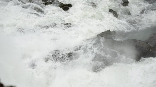 Close tracking shot of majestic waterfalls careening over river rocks forming white water rapids.