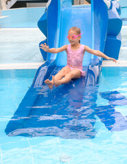 Child sliding into the water in aqua park. Kid having fun and entertaining in indoor swimming pool....