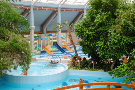 Water fountain in aquapark. Mushroom shape fountain in indoor adventure park full of green palm trees with bridge and swimming pools, hydro massage tubs indoor
