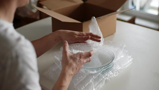 Rear view of unrecognizable man pack up breakable fragile glassware into wrapping bubble plastic and put into cardboard box in preparation to move to new home. Closeup of male preparing to relocation.