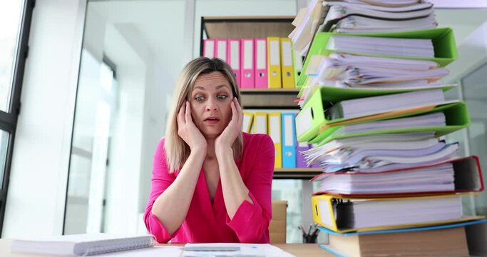 Woman clutches head looking at enormous stack of folders