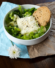 Fresh green salad topped with a large piece of feta cheese and served with a slice of whole grain bread.