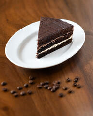 A piece of chocolate cake with white cream, sprinkled with chocolate chips on a plate, decorated with coffee beans.