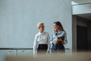Two business women having a discussion as they walk together in a modern office