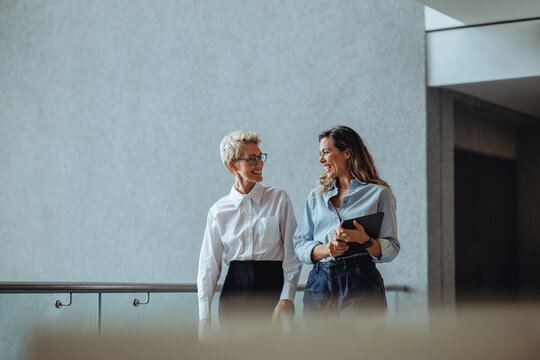 Two business women having a discussion as they walk together in a modern office
