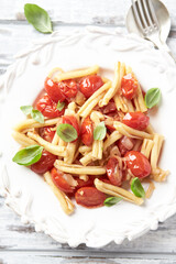 Casarecce pasta withe cherry tomatoes and fresh basil. Bright wooden background. Top view. Close up.