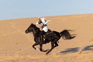 Saudi man in a desert, riding a black stallion, shooting a hunting rifle