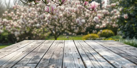 Schilderijen op glas An empty old light grey wooden table with a garden with a blooming magnolia in the background © Veayo