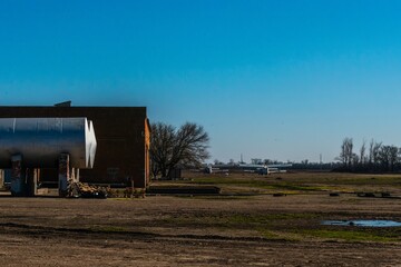 rural aviation field airfield with a biplane on the airfield, a brick barn and a refueling tank in...