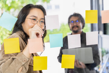 Business team meeting planning new strategy using colored sticky notes on mirror board in workplace.